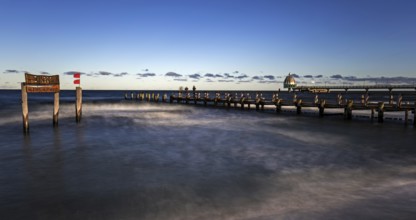 Wooden sign in the sea with inscription Zingst and wooden walkway, pier with diving gondola behind,