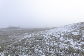 Mystical Celtic burial mounds in winter fog near Erkenbrechtsweiler. Snowy historic burial sites on