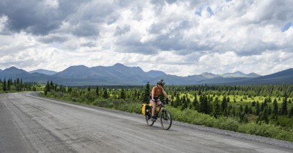 Young woman riding a bicycle on a dirt road through the tundra, mountainous landscape, Denali Park