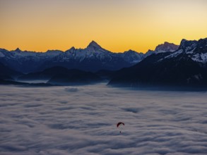 Paragliding flies over a sea of fog, behind Berchtesgaden Alps with Watzmann, Hochkalter and