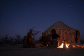 Himba at the campfire in the evening, night view, Himba huts, traditional Himba village in the