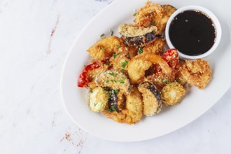 Shrimp and assorted vegetables are deep fried in a light batter and served on a white plate. A