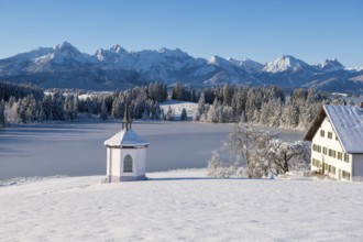 Snowy landscape with chapel, farm and mountains in the background under clear sky, Hegratsrieder