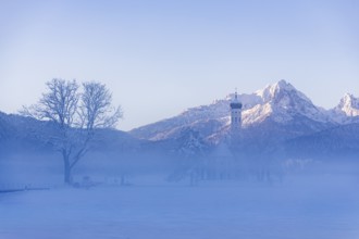 Snowy mountain landscape with St. Coloman pilgrimage church in the foreground and foggy background,