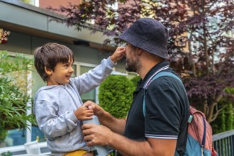 Playful preschool child touching his father's nose while holding a water bottle in a residential