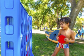Young boy concentrating on playing a giant connect four game in a park on a summer day, holding a