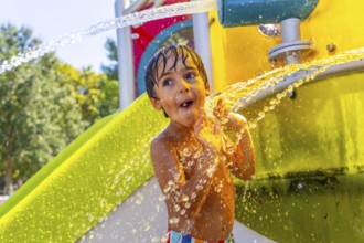 Young boy is having fun playing under refreshing water jets at a colorful water park in kamloops,