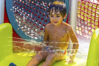 Young boy is having fun playing and splashing in the water jets at a colorful splash park in