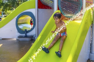 Happy child enjoying a sunny summer day, sliding down a bright green water slide at a splash park,