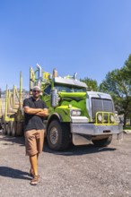 Truck driver standing with arms crossed in front of his logging truck on a sunny day in kamloops,