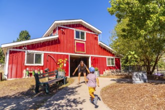 Child runs towards their mother who is waiting with open arms in front of a bright red barn at the
