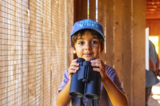 Curious child in a blue cap with good vibes holding binoculars, exploring nature and observing