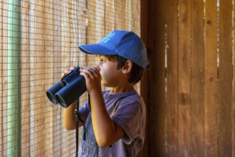 Young boy wearing a blue cap observing wildlife through binoculars at a nature park in kamloops,
