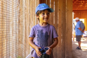 Young boy in a blue cap, holding binoculars, observing animals at british columbia wildlife park in