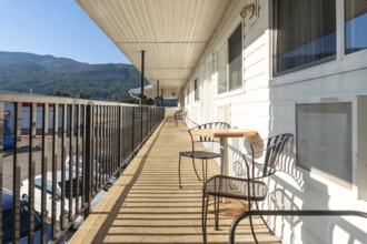 Metal chairs and a small table sit on a motel balcony overlooking a parking lot and a mountain