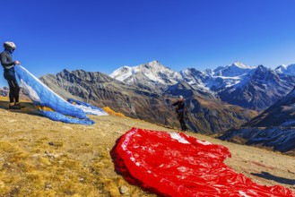 Paragliders are preparing for their start, with the snow-capped peaks of the Valais Alps, Val