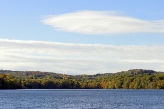 View over Lake Möhnesee, mixed autumn forest on the shore, blue sky, Möhnetalsperre, North