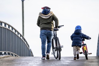Father and son push their bikes up a steep bicycle bridge together