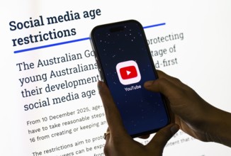 In this photo illustration, a person holds a phone displaying the YouTube app in front of a screen