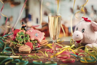Filled champagne glass surrounded by New Year cookies, streamers and plush pig