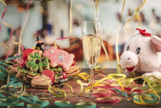 Pour sparkling wine into glass surrounded by New Year cookies, streamers and a plush pig