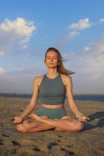 A woman performs Ashtanga Vinyasa yoga in Padmasana with Chin mudra on the beach, meditating