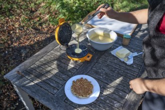 Preparation of waffles with a waffle iron on an outdoor garden table, Othenstorf,