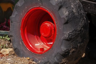 Close-up and rear side view of large heavy duty black rubber tire mounted on red rim on monster