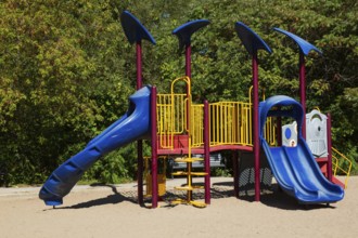 Kids playground equipment with slides, climbers and monkey bars installed in sandy ground in city