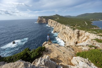 Tourist enjoying the view of steep cliffs by the sea, coastal landscape, cliffs on the Capo Caccia