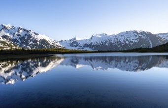 Mountain peaks with Portage Glacier glacier and snow reflected in Divide Lake mountain lake in