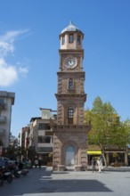 A tall clock tower in an urban square with trees and shops, Çanakkale Clock Tower, Canakkale,