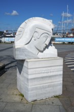 A marble sculpture with the inscription 'Troia' on the harbor, boats in the background, Çanakkale,