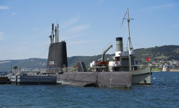 Submarine and ship in harbor overlooking a distant city and hills, TCG Uluçalireis S-338, War