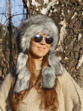 Slender pretty woman with Mongol hat, red hair and warm winter colors between birch forest and