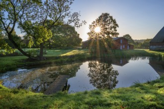 Manor with historic stables and pond, from 1923, in backlight with sun star, Gut Othenstorf,