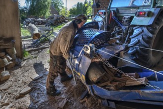 Young man sawing and splitting beech logs with his saw cutting machine, powered by a tractor in a