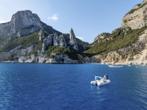 Couple on motorboat off picturesque rocky coast, cliffs with L'Aguglia pinnacle, blue sea and Cala