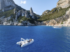 Motor boat off picturesque rocky coast, cliffs with L'Aguglia pinnacle, blue sea and Cala Goloritzé