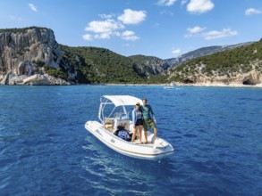 Couple, young woman and young man on motor boat off picturesque rocky coast, cliffs and Cala Luna
