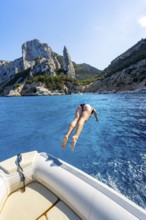 Young woman jumping from a boat into the water, picturesque rocky coast, cliffs with L'Aguglia rock