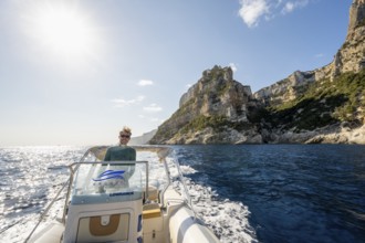 Young man rides a motorboat along the picturesque rocky coast, cliffs and blue sea, Golfo di