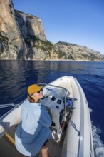 Young woman riding a motorboat along the picturesque rocky coast, cliffs and blue sea, Golfo di