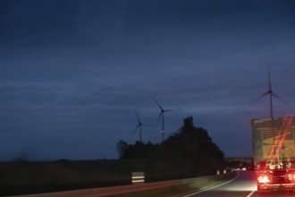 Truck on federal highway at night, wind turbine lights on the left, Schleswig-Holstein, Germany