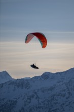 Paragliders flying over snowy mountain peaks in winter in evening light, Kitzbühel Alps, Tyrol,
