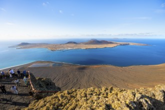 View of La Graciosa island with volcanic craters in the evening light, tourists on an observation