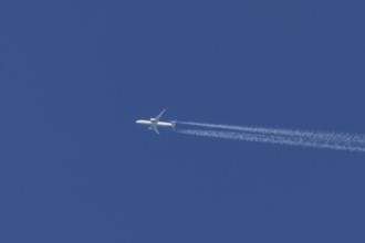 Jet passenger aircraft flying in a blue sky with contrails or vapour trails behind, England, United