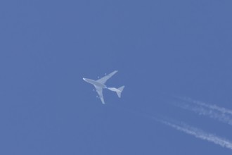 Boeing 747 jumbo jet cargo aircraft flying in a blue sky with contrails or vapour trails behind,