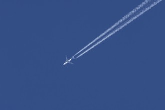 Jet passenger aircraft flying in a blue sky with contrails or vapour trails behind, England, United