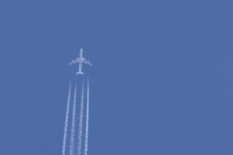 Jet passenger aircraft flying in a blue sky with contrails or vapour trails behind, England, United